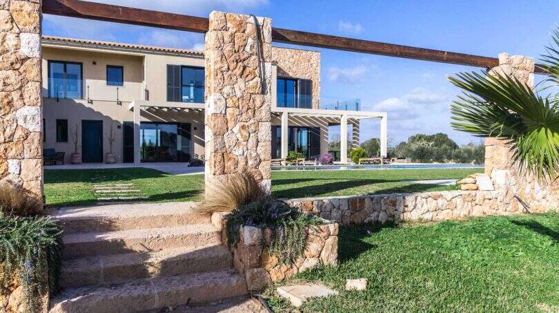 Luxusfinca Ses Salines: Außenansicht mit Natursteinmauern, Poolbereich und gepflegtem Rasen unter blauem Himmel