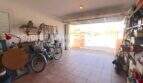 Geräumige Garage mit Rolltor, Fahrrädern, Werkzeugregalen und Ausblick auf den sonnigen Außenbereich.