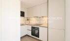 Moderna cocina integrada blanca con horno, microondas y placa de cocción en apartamento esquinero de nueva construcción en Cala Millor