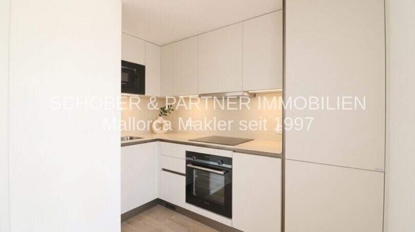 Moderna cocina integrada blanca con horno, microondas y placa de cocción en apartamento esquinero de nueva construcción en Cala Millor