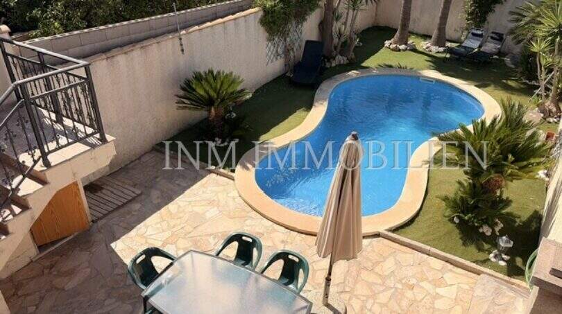 Außenbereich des Ferienhauses in Muro mit Pool, Gartenanlage und überdachter Terrasse mit Sitzgruppe.