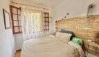 Dormitorio luminoso con cabecero de bambú, ropa de cama blanca y ventanas de madera con vista al mar en Sa Ràpita