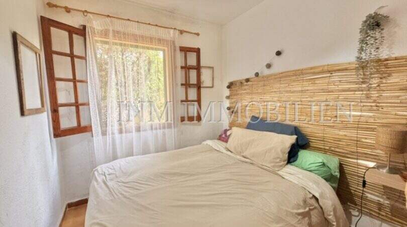 Dormitorio luminoso con cabecero de bambú, ropa de cama blanca y ventanas de madera con vista al mar en Sa Ràpita