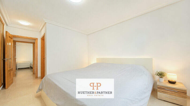 Helles Schlafzimmer der Erdgeschosswohnung Cala Antena mit Doppelbett, Holztüren und modernem Nachttisch.