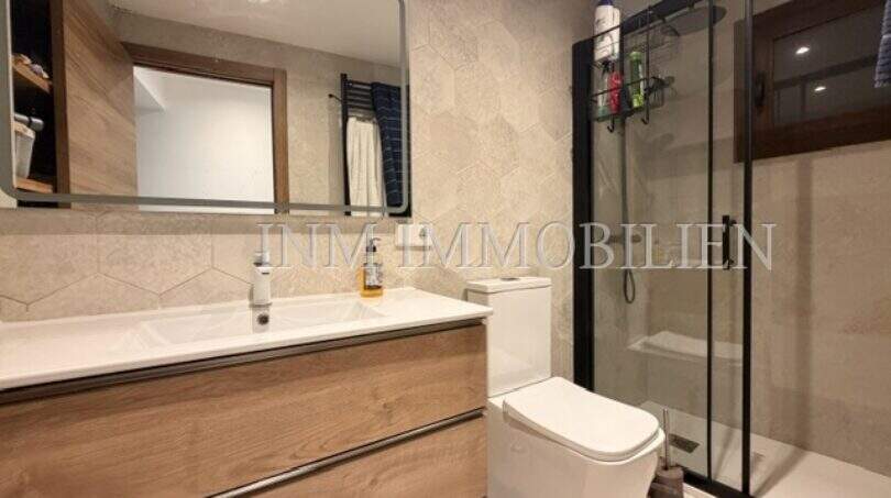Modernes Badezimmer mit Holzunterschrank, Glasdusche und Hexagon-Wandfliesen in sanierter Wohnung in Pere Garau