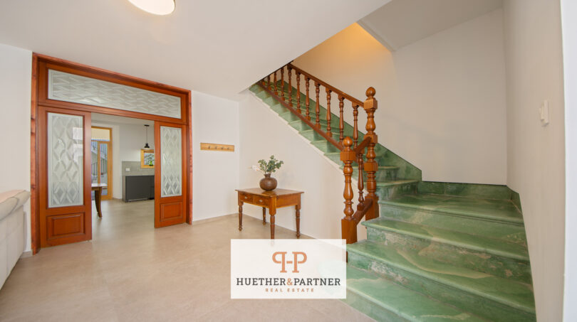 Eingangsbereich mit grüner Marmortreppe, Holzgeländer und eleganter Glastür im Stadthaus Manacor