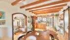 Comedor rústico con techo de vigas de madera, mesa de comedor y paso abierto a la cocina en casa mediterránea Sa Ràpita