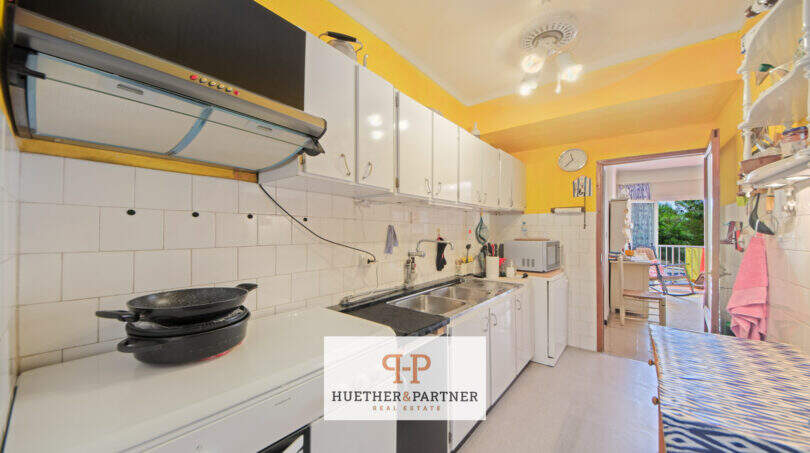 Cocina del apartamento vacacional Porto Cristo con paredes amarillas, armarios blancos y paso a la terraza con vistas al mar