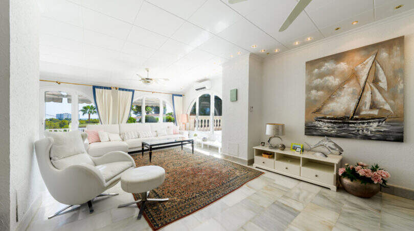 Helles Wohnzimmer der Poolvilla in Cala Murada mit Marmorboden, weißen Sofas und Segelboot-Gemälde.
