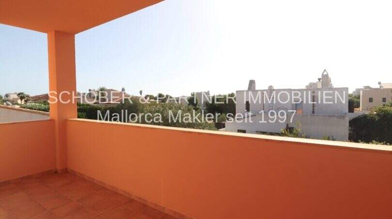 Sonnige Dachterrasse mit orangefarbener Brüstung und Blick über die Dächer von Sa Coma in Meeresnähe.