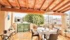 Terraza cubierta con vigas de madera, mesa de comedor y vista al jardín de la casa mediterránea en Sa Ràpita