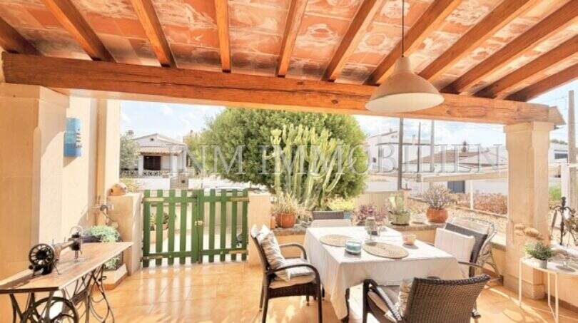 Terraza cubierta con vigas de madera, mesa de comedor y vista al jardín de la casa mediterránea en Sa Ràpita