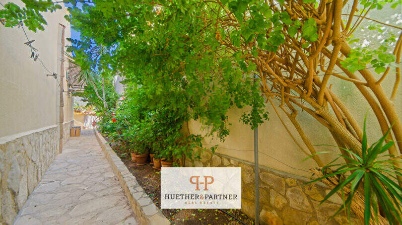 Gepflegter Gartenweg mit Natursteinpflaster, üppiger Begrünung und Topfpflanzen an der Hauswand in Cala Murada.