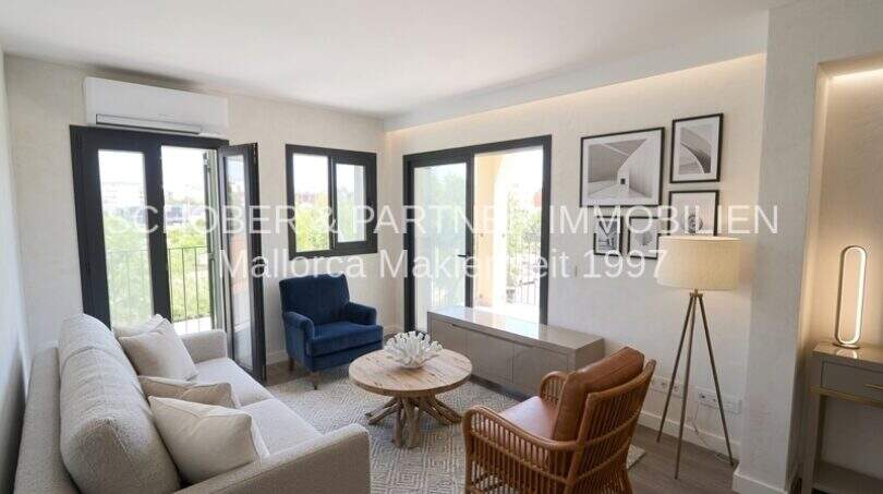 Área de estar clara del apartamento esquinero de nueva construcción en Cala Millor con sofá moderno, sillón de ratán y puertas balconeras.