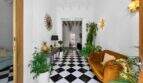 Elegante entrada con piso de tablero de ajedrez, acentos dorados, sofá de terciopelo y plantas de interior en casa urbana Felanitx