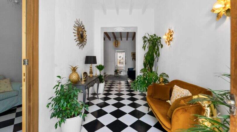 Elegante entrada con piso de tablero de ajedrez, acentos dorados, sofá de terciopelo y plantas de interior en casa urbana Felanitx