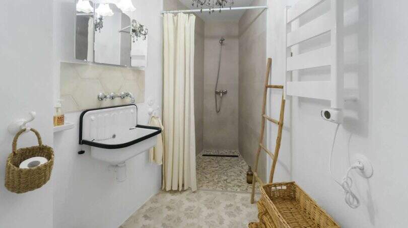 Baño luminoso con lavabo vintage, ducha, lámpara de cristal y cestas de fibra natural en la casa urbana de Felanitx