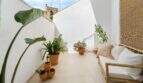 Soleada terraza de azotea con paredes blancas, sofá de bambú, macetas de terracota y plantas de la casa urbana en Felanitx