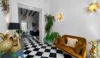 Sala de estar elegante con suelo de ajedrez, sofá de terciopelo dorado y plantas exuberantes en la casa urbana de Felanitx