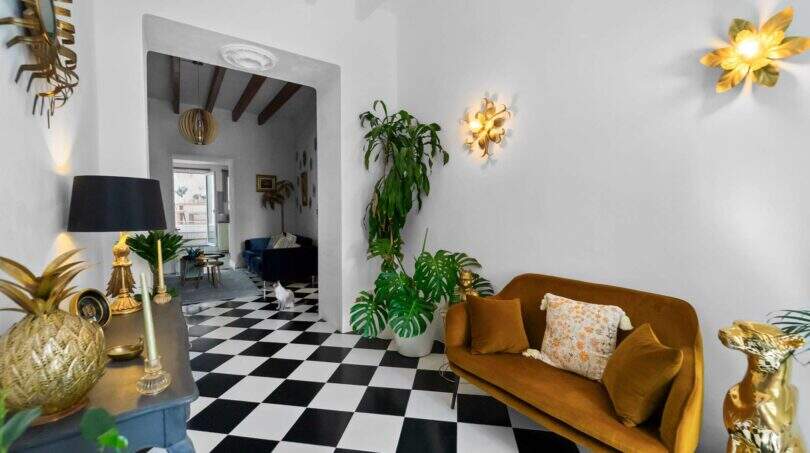 Sala de estar elegante con suelo de ajedrez, sofá de terciopelo dorado y plantas exuberantes en la casa urbana de Felanitx