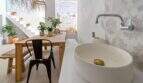Sala de estar abierta con mesa de madera, lavabo, azulejos hexagonales y escalera con plantas en la casa urbana de Felanitx