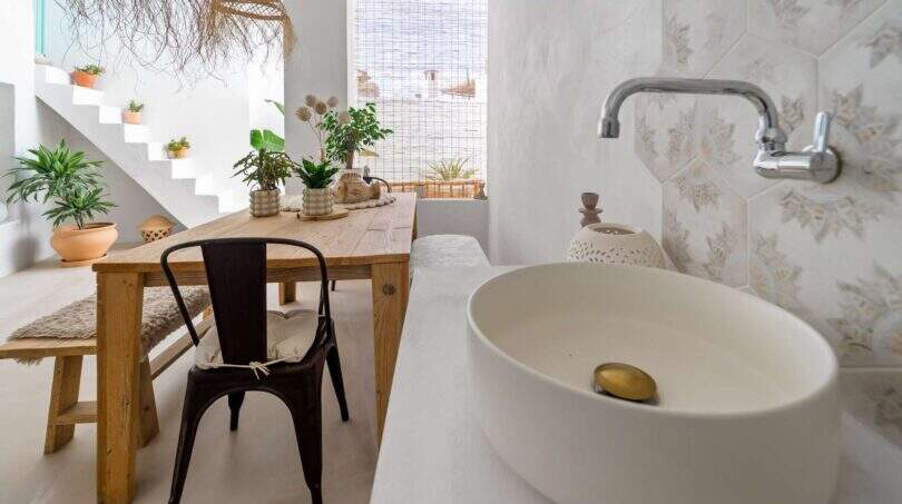 Sala de estar abierta con mesa de madera, lavabo, azulejos hexagonales y escalera con plantas en la casa urbana de Felanitx