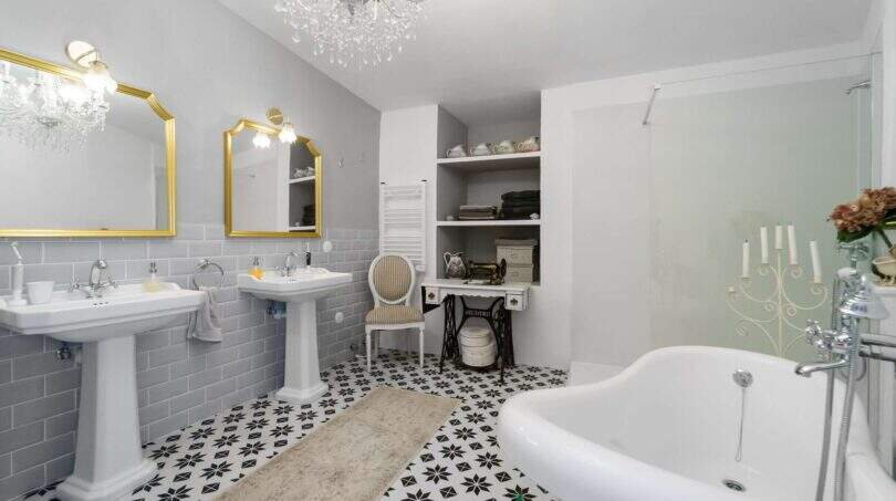 Elegante baño con lámpara de cristal, espejos dorados, bañera exenta y piso de baldosas de mosaico en casa urbana Felanitx