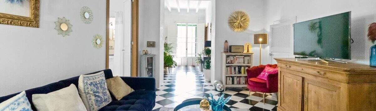 Sala de estar con sofá de terciopelo azul, piso de tablero de ajedrez, techo de vigas de madera y sillón rojo en casa urbana Felanitx