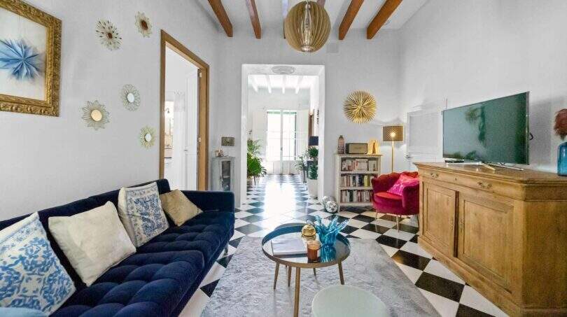 Sala de estar con sofá de terciopelo azul, piso de tablero de ajedrez, techo de vigas de madera y sillón rojo en casa urbana Felanitx