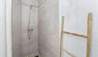 Ducha a nivel del suelo con baldosas efecto hormigón, alcachofa de mano y escalera de madera como toallero en casa urbana Felanitx