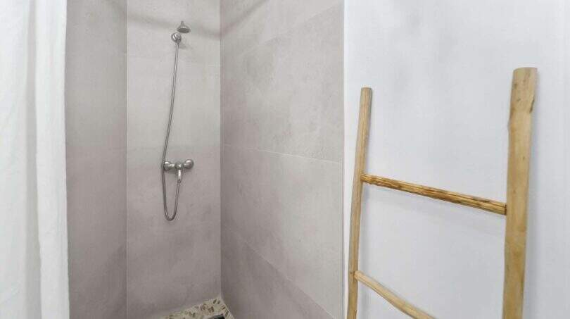 Ducha a nivel del suelo con baldosas efecto hormigón, alcachofa de mano y escalera de madera como toallero en casa urbana Felanitx