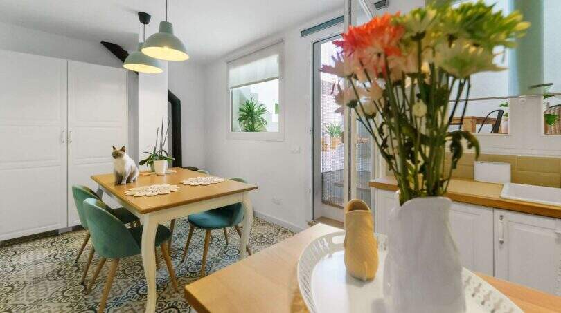 Comedor luminoso con piso de baldosas con patrón, mesa de madera, sillas turquesas y decoración floral en casa urbana Felanitx
