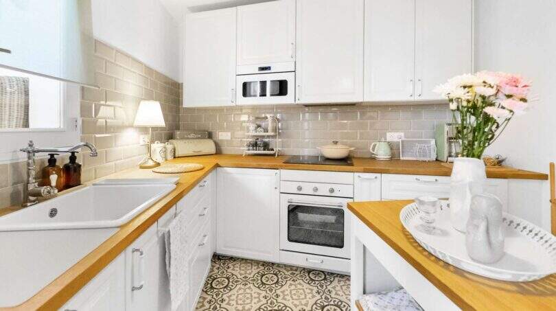 Cocina luminosa con armarios blancos, encimeras de madera, suelo de mosaico y electrodomésticos modernos en la casa urbana de Felanitx
