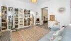 Sala de estar luminosa con gran pared de libros, piso de baldosas con patrón, alfombra vintage y sofá azul claro en casa urbana Felanitx