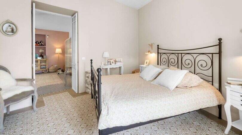 Dormitorio luminoso con cama de hierro forjado, piso de baldosas con patrón y vista a la habitación contigua, casa urbana Felanitx