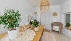 Sala de estar luminosa con mesa de madera, sillón de ratán, plantas de interior y decoración boho en casa urbana Felanitx