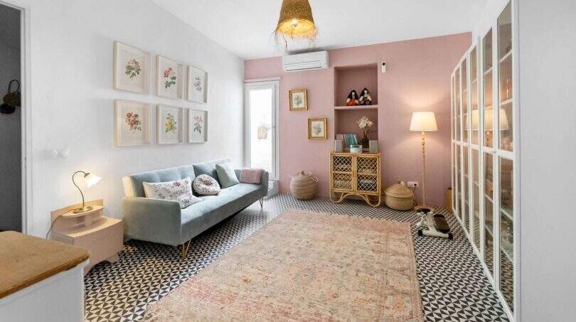 Sala de estar con sofá gris, pared de acento rosa, piso de baldosas con patrón y alfombra vintage en casa urbana Felanitx