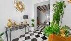 Elegante entrada con piso de tablero de ajedrez, acentos dorados, plantas Monstera y vista al siguiente ambiente
