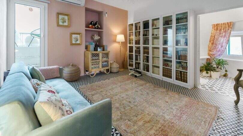 Sala de estar con sofá azul, estantería, piso de mosaico y pared rosa en casa urbana Felanitx