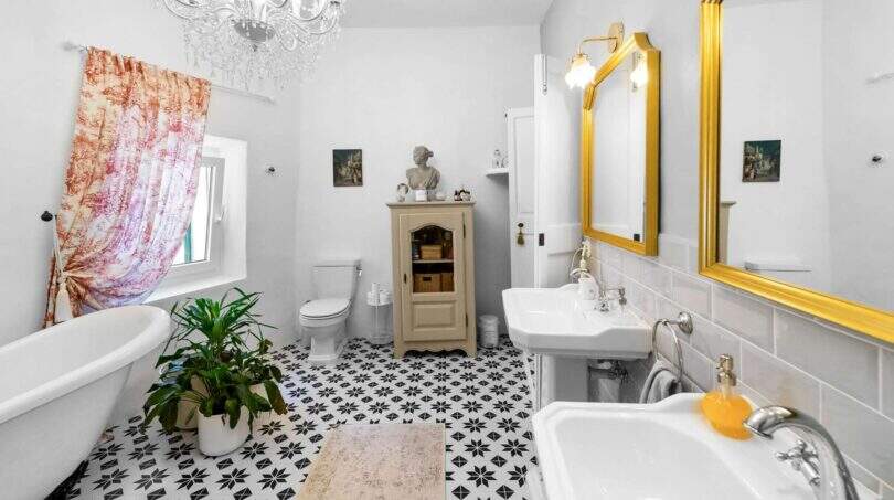 Baño elegante con lámpara de araña, bañera estilo claw-foot, espejo con marco dorado y patrón de azulejos en blanco y negro en la casa urbana de Felanitx