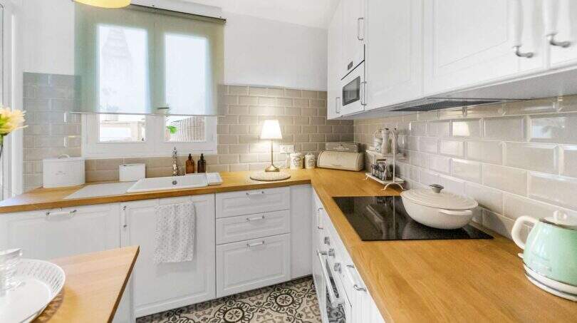 Cocina luminosa con armarios blancos, encimeras de madera, placa de cocción y baldosas de piso con patrón en casa urbana Felanitx