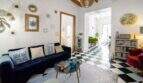 Sala de estar luminosa con piso de tablero de ajedrez, sofá de terciopelo azul, espejos de pared dorados y techo de vigas de madera en casa urbana Felanitx