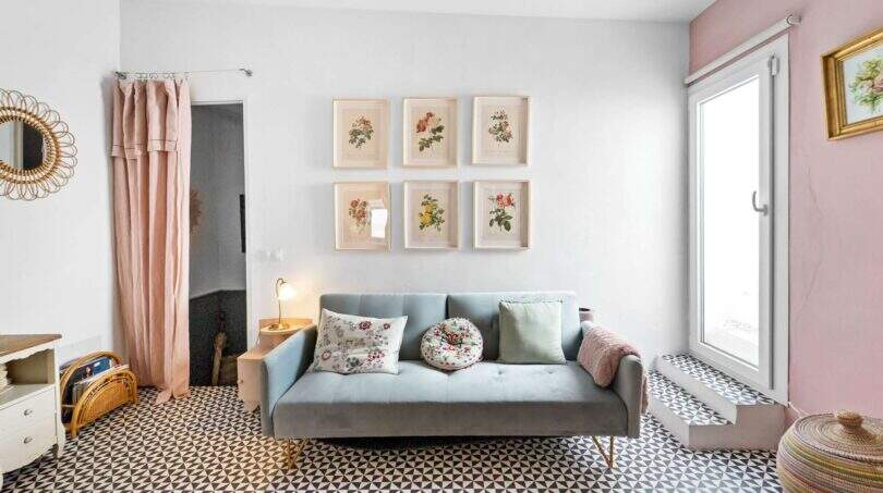 Sala de estar con sofá gris, cuadros de flores, piso de baldosas con patrón y acentos rosa en casa urbana Felanitx