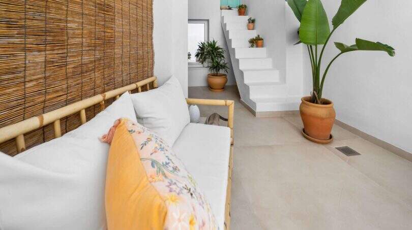 Área de estar con sofá de bambú, escalera blanca y plantas verdes en encantadora casa urbana en Felanitx