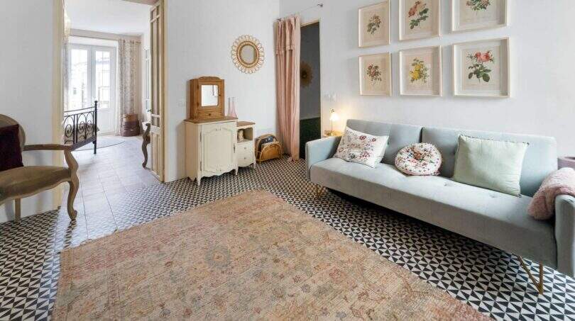 Sala de estar con sofá azul claro, cómoda vintage, cuadros de flores y piso de baldosas con patrón en casa urbana Felanitx