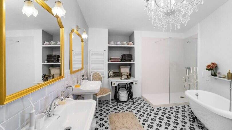 Elegante baño con lámpara de araña, espejos dorados, bañera exenta y piso de mosaico blanco y negro en casa urbana Felanitx