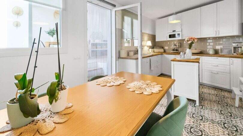 Comedor luminoso con mesa de madera, sillas verdes y cocina abierta con armarios blancos en casa urbana Felanitx