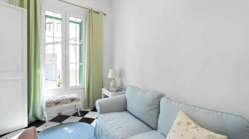 Sala de estar luminosa con sofá azul, cortinas verdes y piso de tablero de ajedrez en casa urbana Felanitx