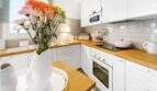 Cocina luminosa con armarios blancos, encimeras de madera, baldosas metro y ramo de flores en casa urbana Felanitx