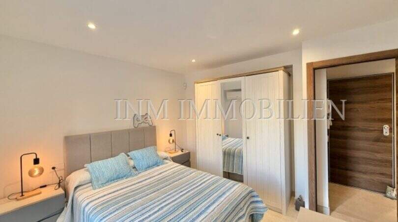 Helles Schlafzimmer mit Doppelbett, blauer Bettwäsche, Einbauschrank und Holztür in möblierter Wohnung in Pere Garau